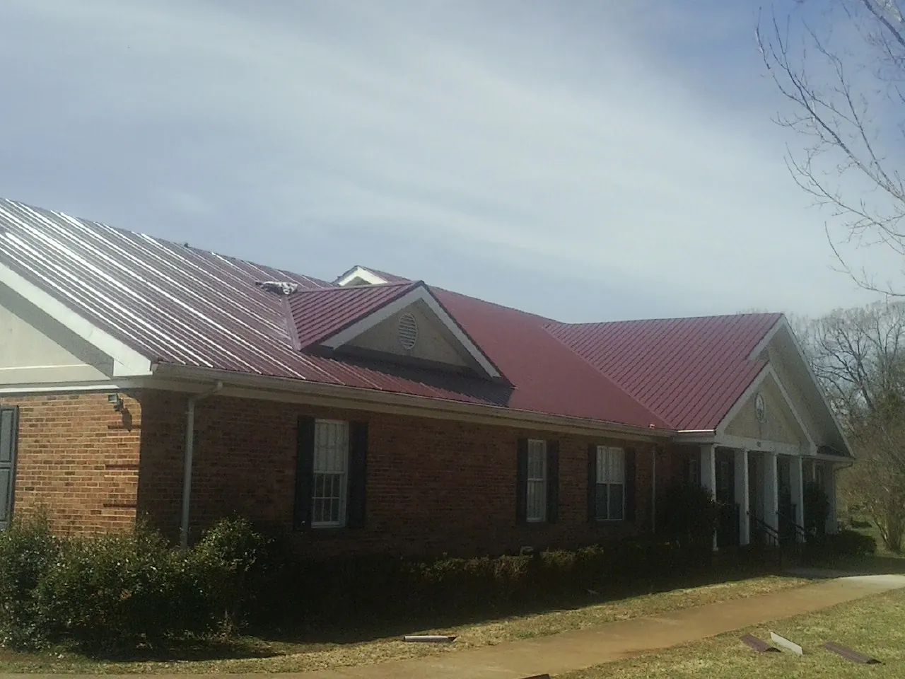 Red metal roof with gabled entries on a long brick building, from a Hail Damage Roof Repair job in Whitesville