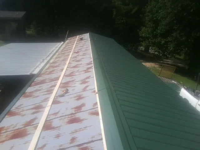Old rusted panels beside newly installed green metal roofing — Wind Damage Roof Repair by Roofing Brothers in Whitesville