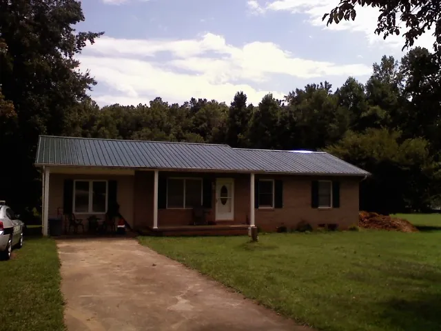 Dark green metal roof on a brick ranch with a covered porch in Whitesville