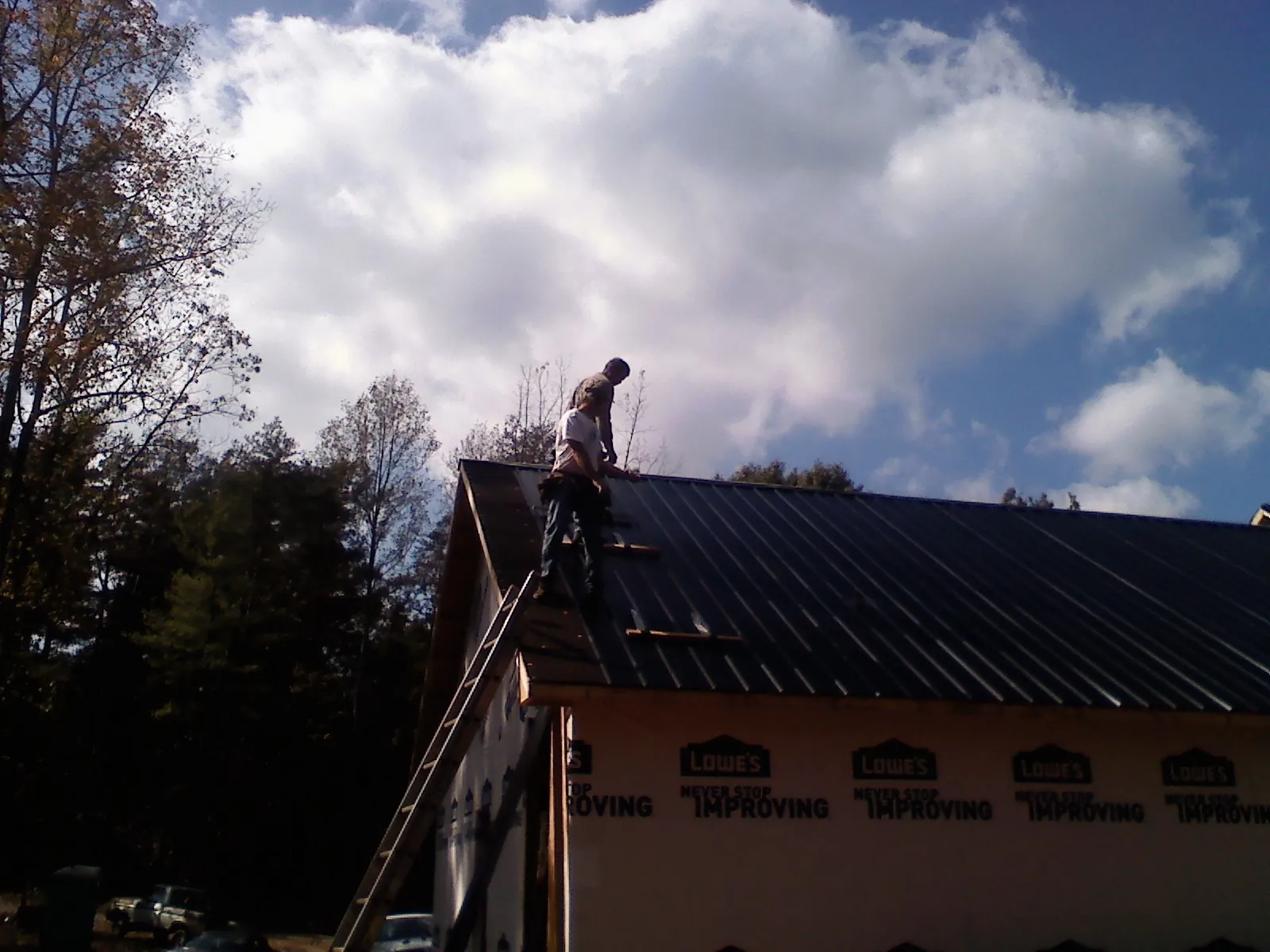 Roofer fastening dark metal panels high against a cloudy sky, from a Roof Inspection job in Whitesville