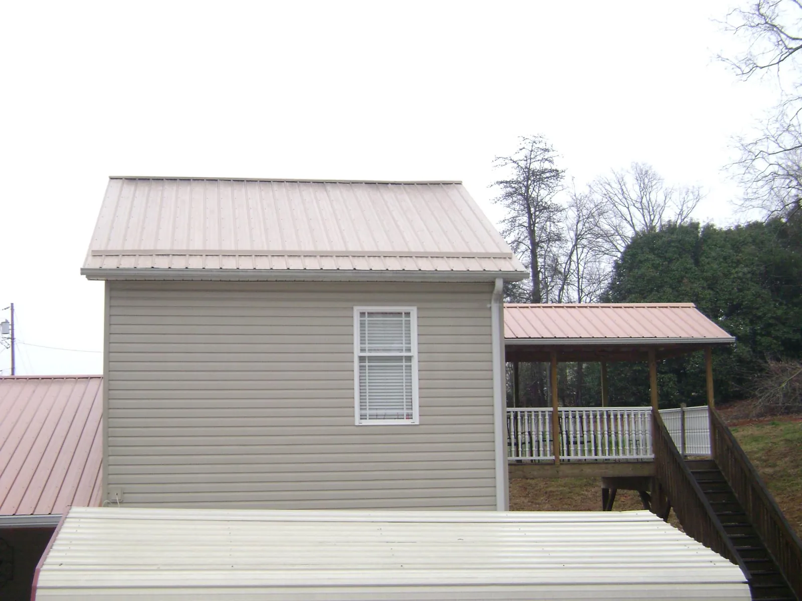 Tan metal roofs on a two story addition and attached porch, from a Roof Replacement job in Whitesville