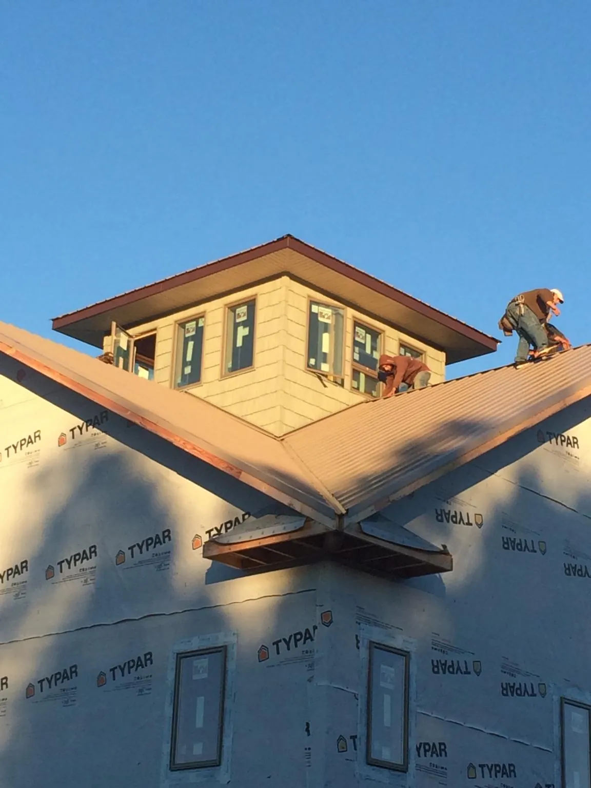 Roofers working around a rooftop cupola on a new metal roof at sunset — Roof Waterproofing in Whitesville by Roofing Brothers